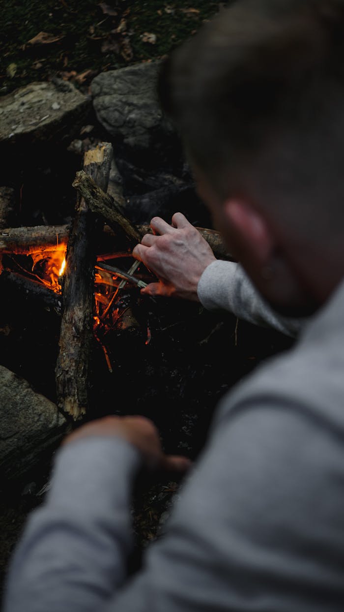 Home A man skillfully starts a campfire with wooden logs, emphasizing survival skills.